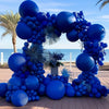 A large balloon arch garland made of royal blue balloons set up outdoors on a wooden deck.