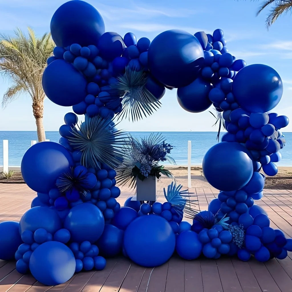 A large balloon arch garland made of royal blue balloons set up outdoors on a wooden deck.