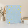 A light blue laminated photo album with small yellow heart accents sits on a white surface.