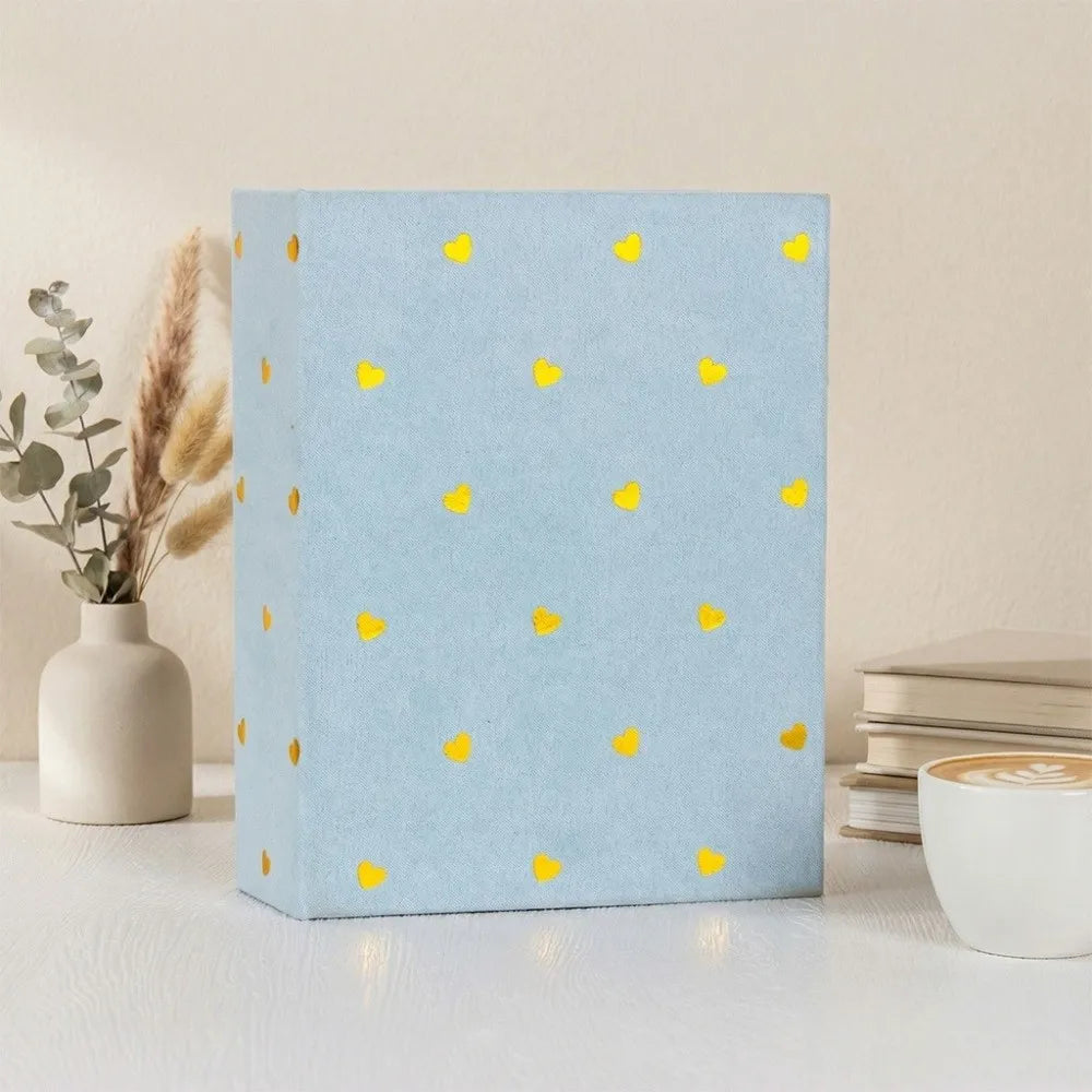 A light blue laminated photo album with small yellow heart accents sits on a white surface.