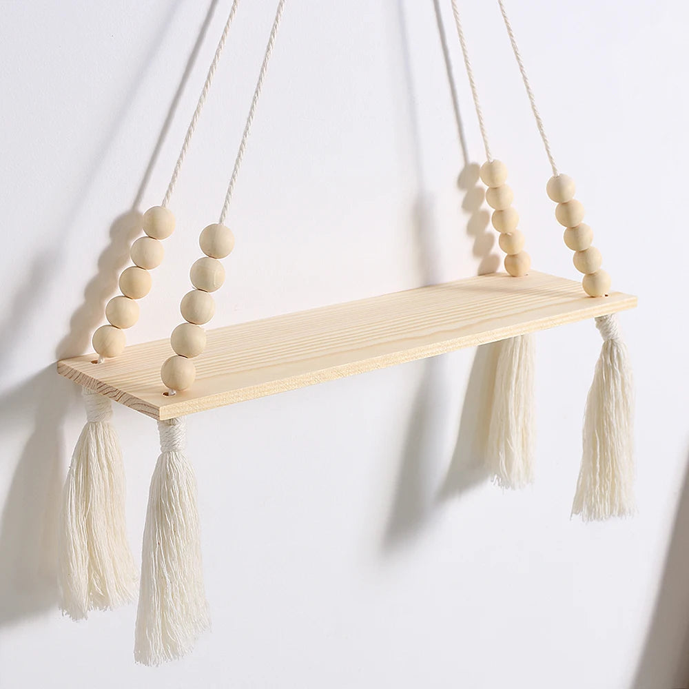 A rustic wooden wall shelf with macrame tassels hangs against a white wall.