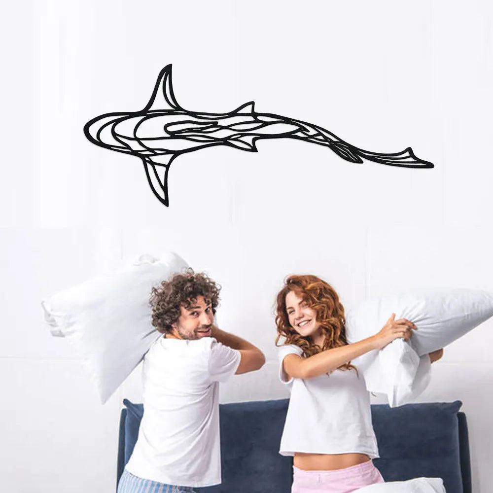 A woman and a man are looking at a black line sculpture of a shark on a white wall.