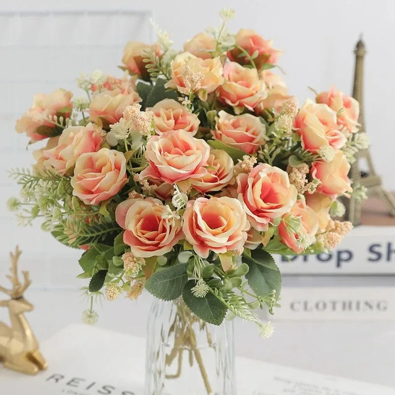 A bouquet of peach and pink silk touch artificial roses with greenery displayed in a glass vase.