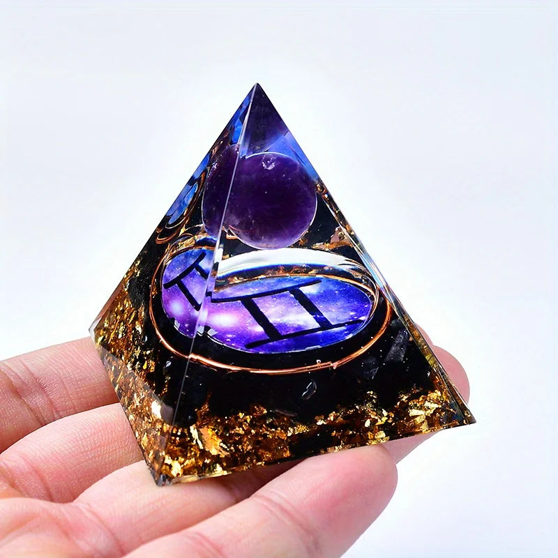 A clear quartz pyramid with an iridescent purple and gold design is held in a hand.