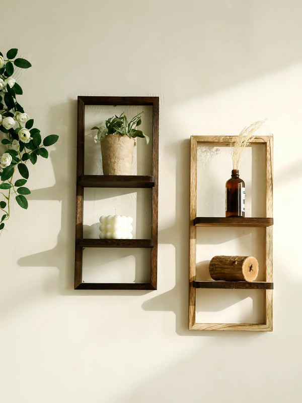 A rustic wooden floating shelf with two tiers displaying a potted plant and a glass bottle on a light-colored wall.