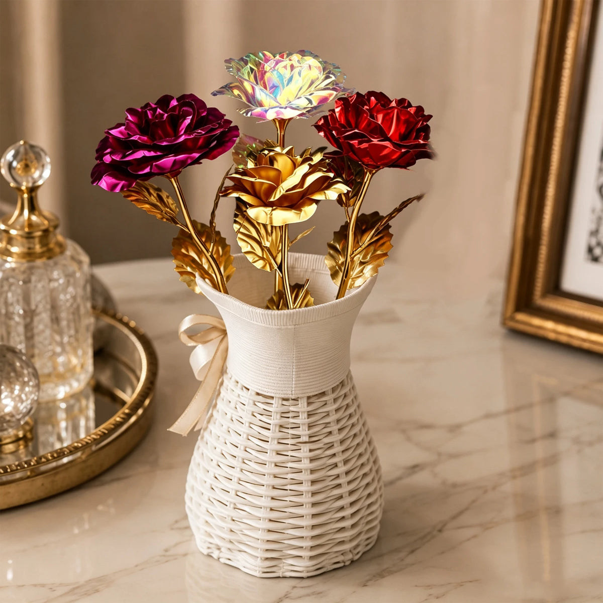 A bouquet of iridescent gold foil roses in deep magenta and red are displayed in a white woven vase.