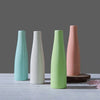 Three ceramic mini vases in pastel shades of mint green, white, and pink standing upright on a light wooden surface.
