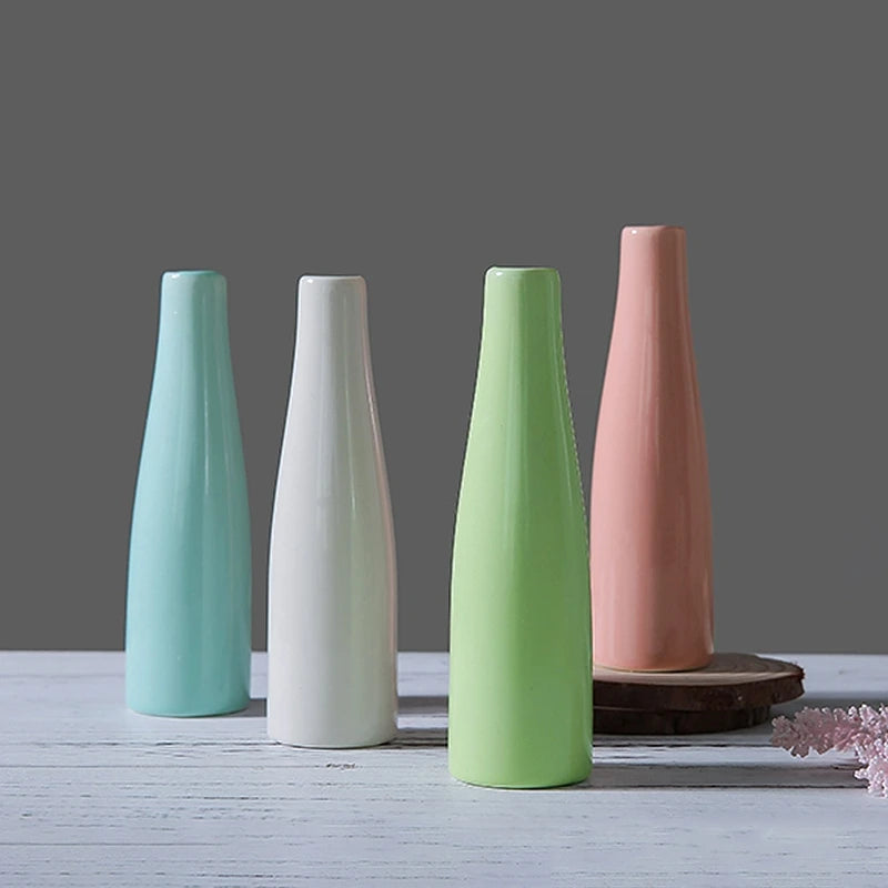 Three ceramic mini vases in pastel shades of mint green, white, and pink standing upright on a light wooden surface.