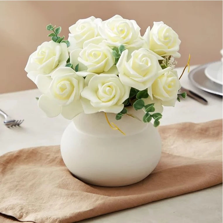 A bouquet of white artificial foam roses in a white vase on a beige linen cloth.