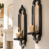 A dark wooden wall shelf with an arched design holds two pillar candles and a small gold star decoration.