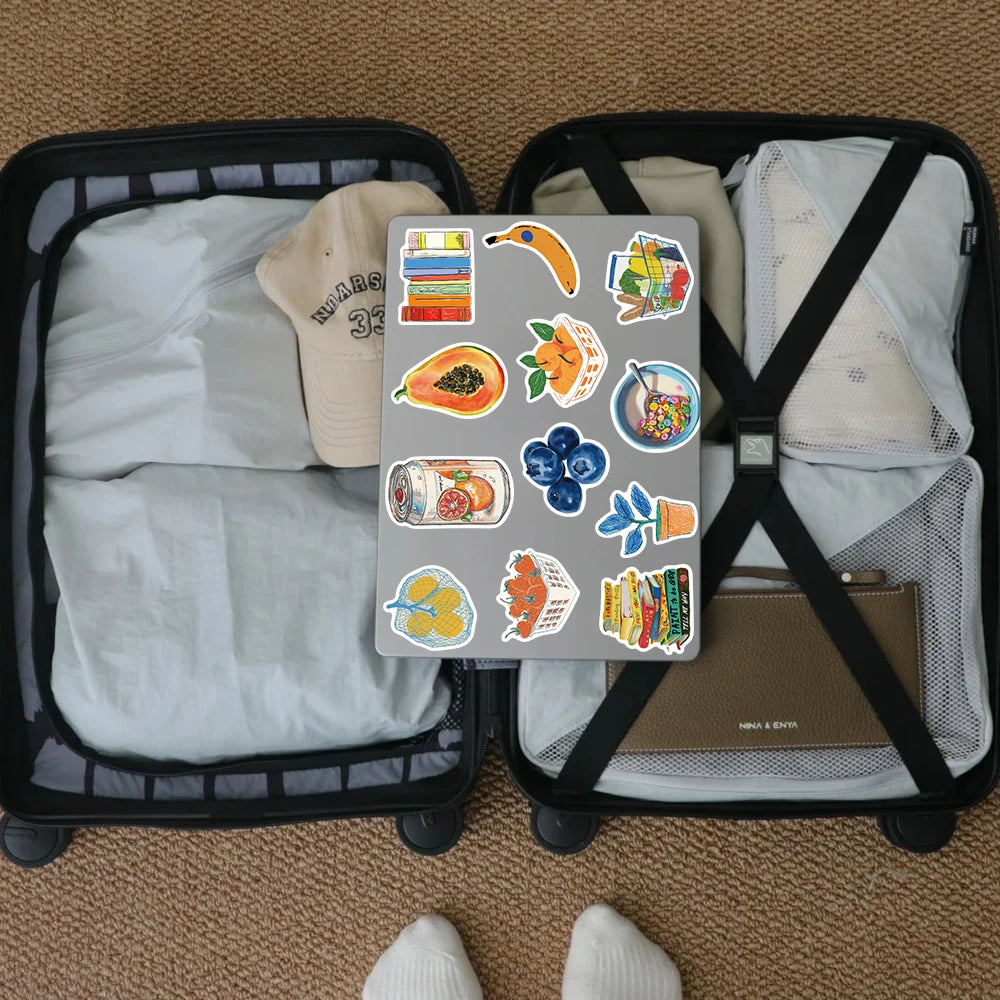 A pack of watercolor food and fruit stickers is displayed inside a black storage basket with soft fabric items.