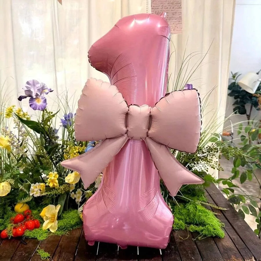 A large pink balloon shaped like the number one with a matte bow, displayed among greenery.