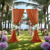 An outdoor wedding backdrop featuring orange chiffon curtains framing a lush garden and palm trees.