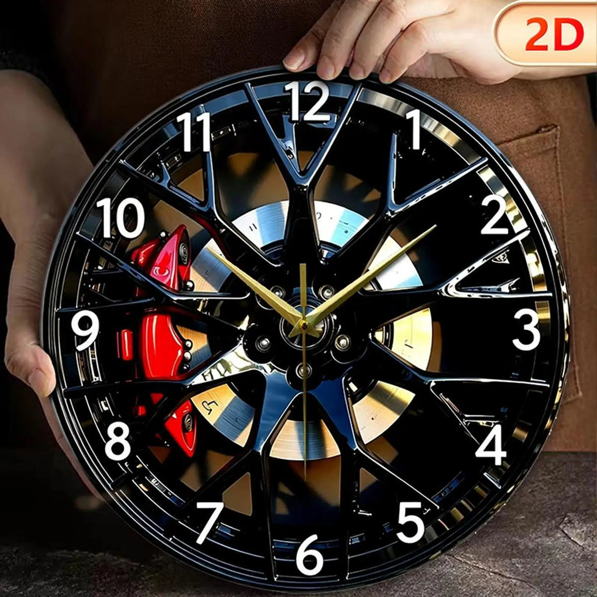 A close-up of a black and gold creative 2D tire wheel acrylic wall clock being held by a hand.