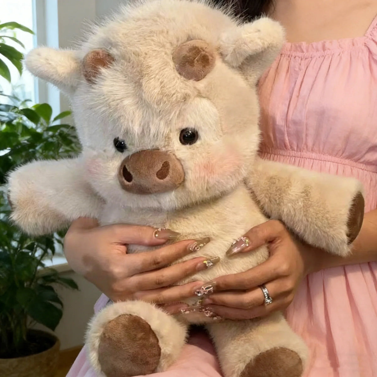 Une personne tient une peluche de veau écossais moelleuse et de couleur claire.