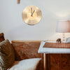 A round, gold-toned vinyl record wall clock hangs on a white wall above a wooden cabinet and a light-colored table.