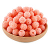 A pile of small, pink textured resin beads for jewelry making in a wooden bowl.