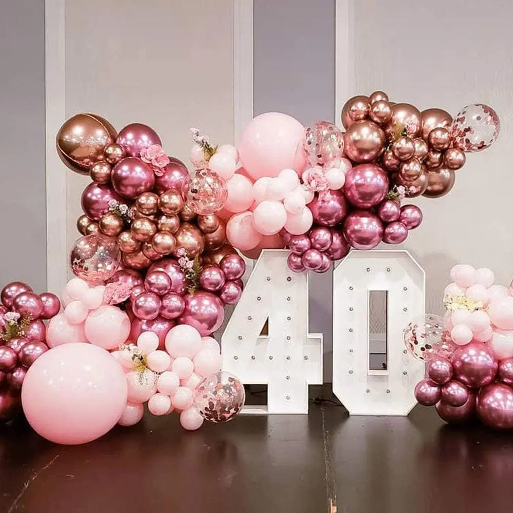 A large balloon arch decoration featuring metallic pink and rose gold latex balloons for a celebration.