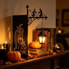 A black silhouette of a witch and cauldron on a lighted sign with a warm lantern hanging above a stack of books.