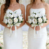 Two brides in white dresses hold bouquets of white roses and greenery.