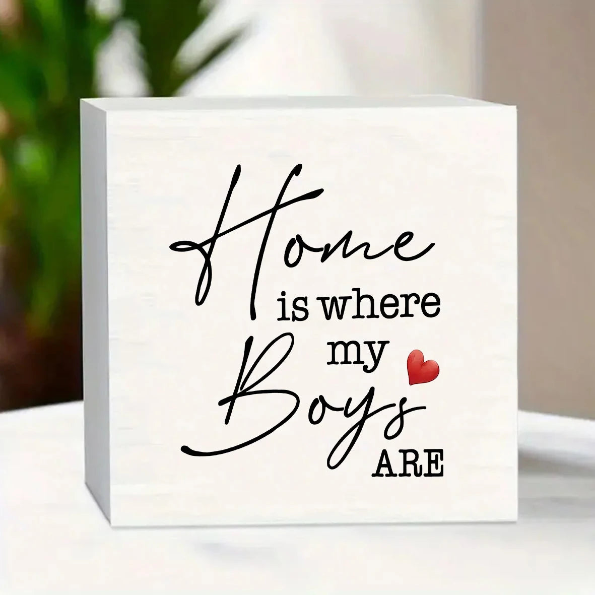 A white wooden sign with black script that reads Home is where my Boys are and a small red heart.