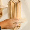 A hand is placing a wooden geometric wall shelf onto a white wall.