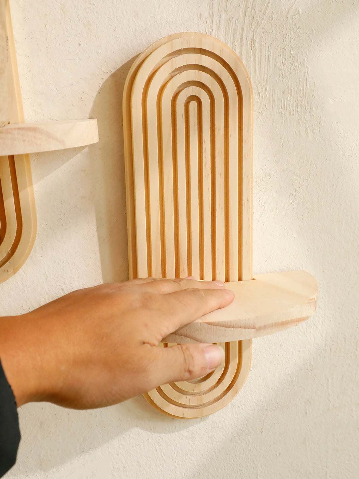 A hand is placing a wooden geometric wall shelf onto a white wall.