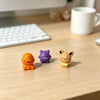 A set of three small, colorful kawaii anime fantasy creature figurines on a wooden desk.
