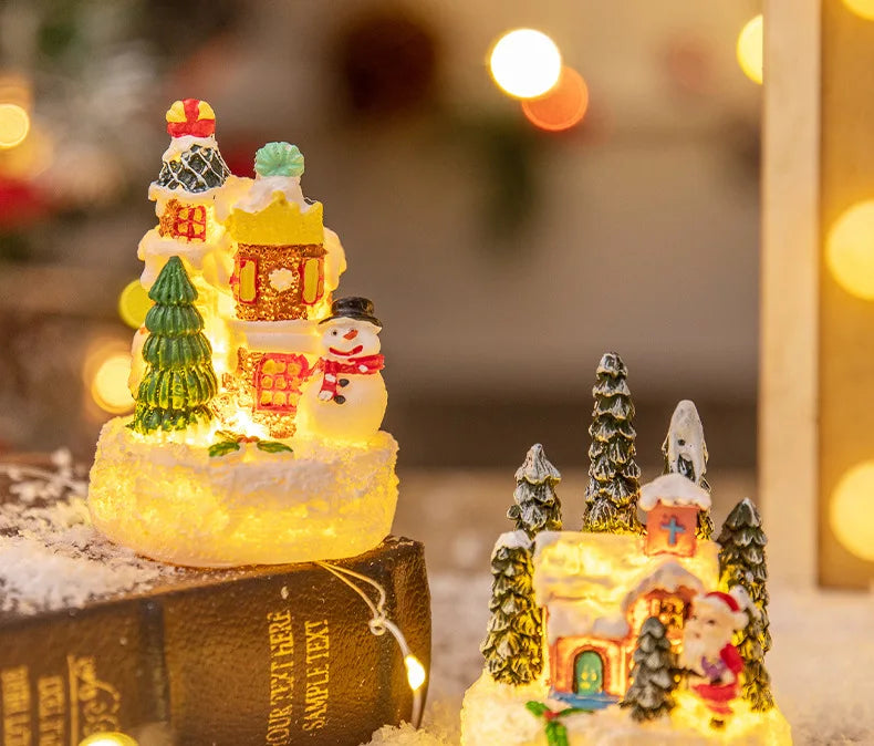 A festive Christmas gingerbread house resin ornament set displayed on a book with warm glowing lights.