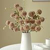 A bouquet of dried, round, dusty pink silk chrysanthemum artificial flowers in a white vase.