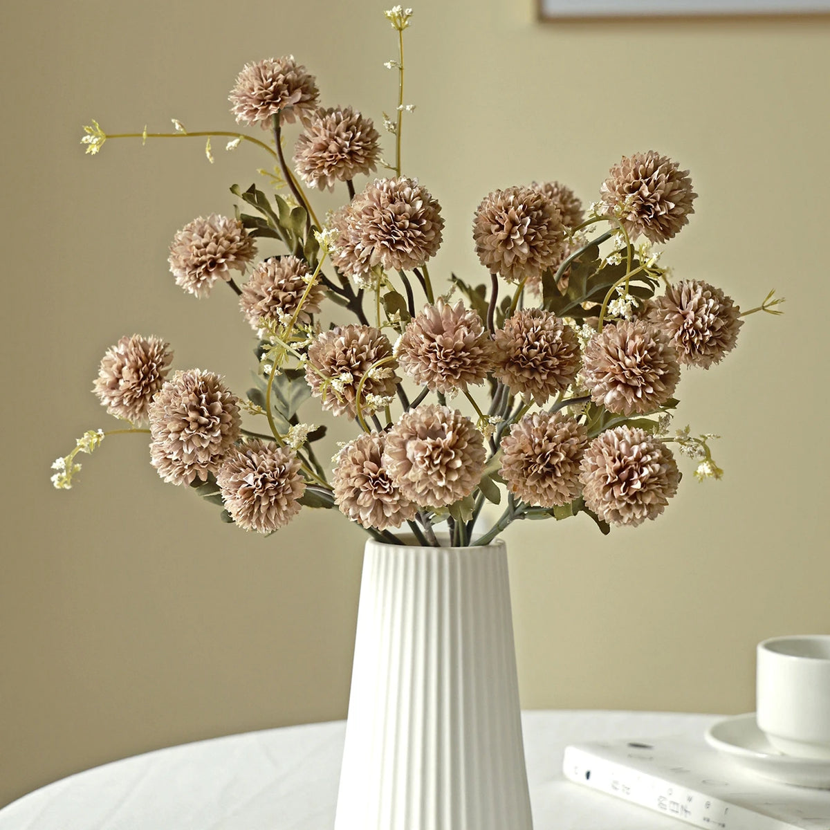 A bouquet of dried, round, dusty pink silk chrysanthemum artificial flowers in a white vase.