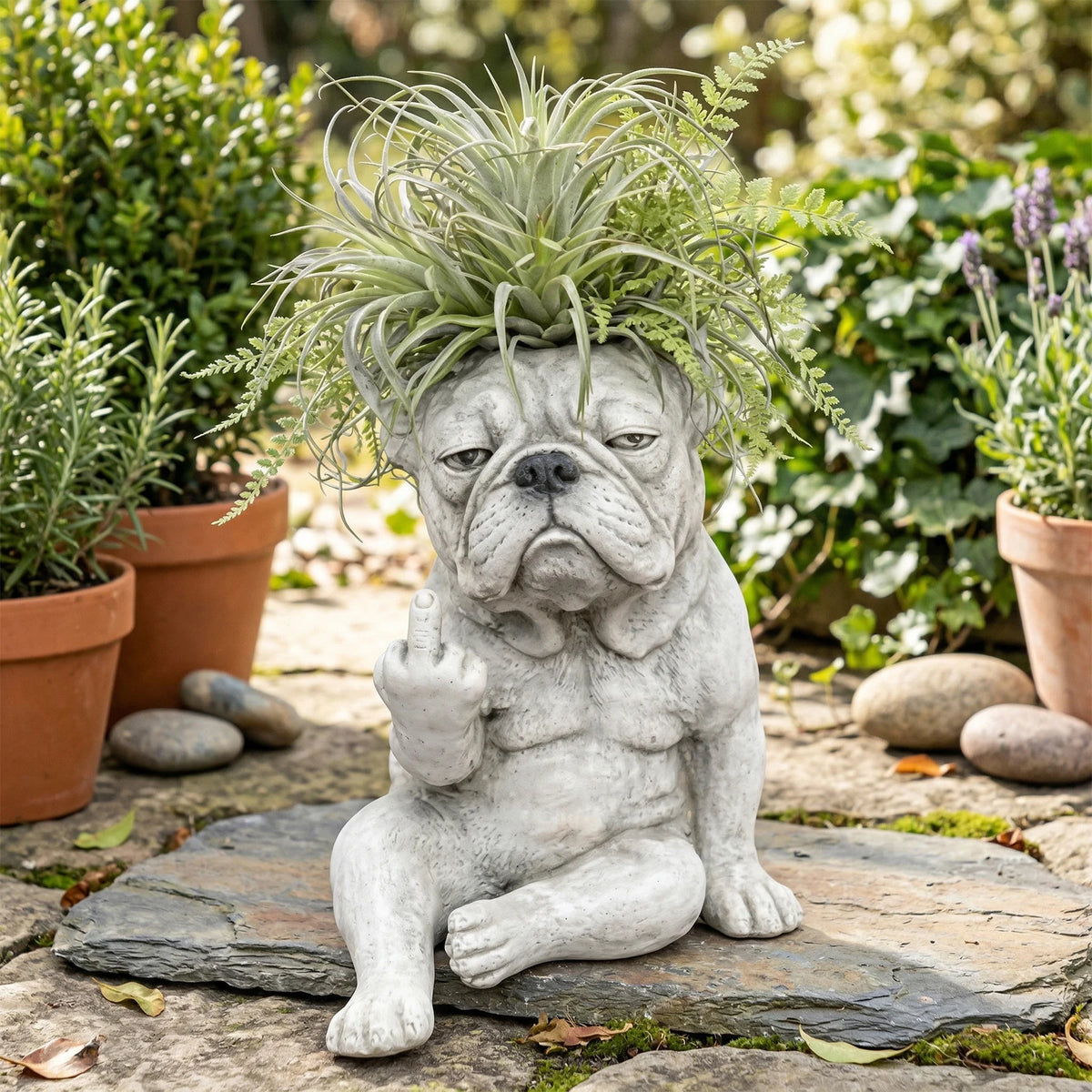 Statue en résine grise d'un bouledogue français avec des feuillages verts pointus, assis sur une dalle de pierre.
