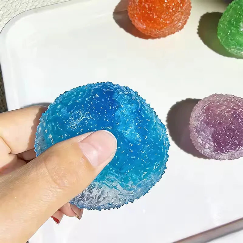 A hand is squeezing a bright blue sensory stress reliever ball on a white plate, with other colored balls visible.