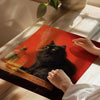 A hand places a glass next to a black cat smoking poster wall art on a wooden surface.
