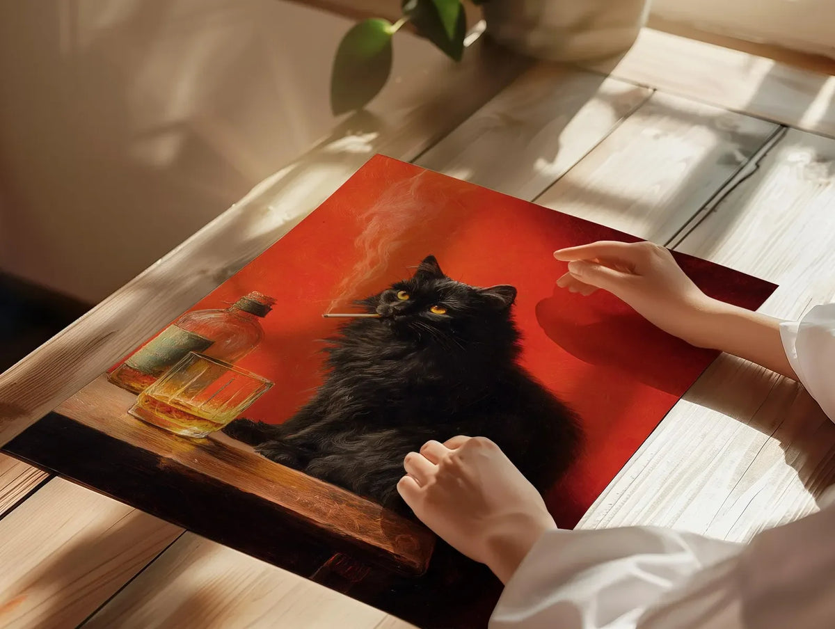 A hand places a glass next to a black cat smoking poster wall art on a wooden surface.