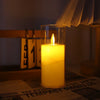 A tall glass candle with a flickering flame is lit in a dark setting.