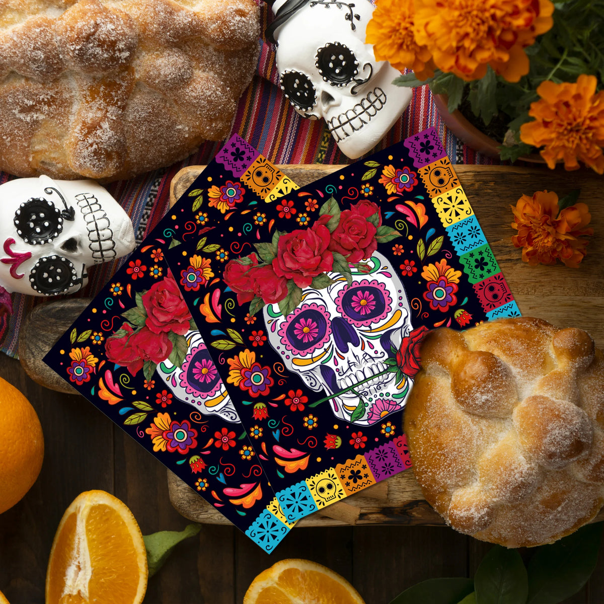 A set of Halloween skeleton and spider paper napkins displayed with pumpkins and baked goods on a wooden board.