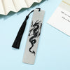 A silver metal bookmark featuring a black dragon design with a black tassel on a light blue background.
