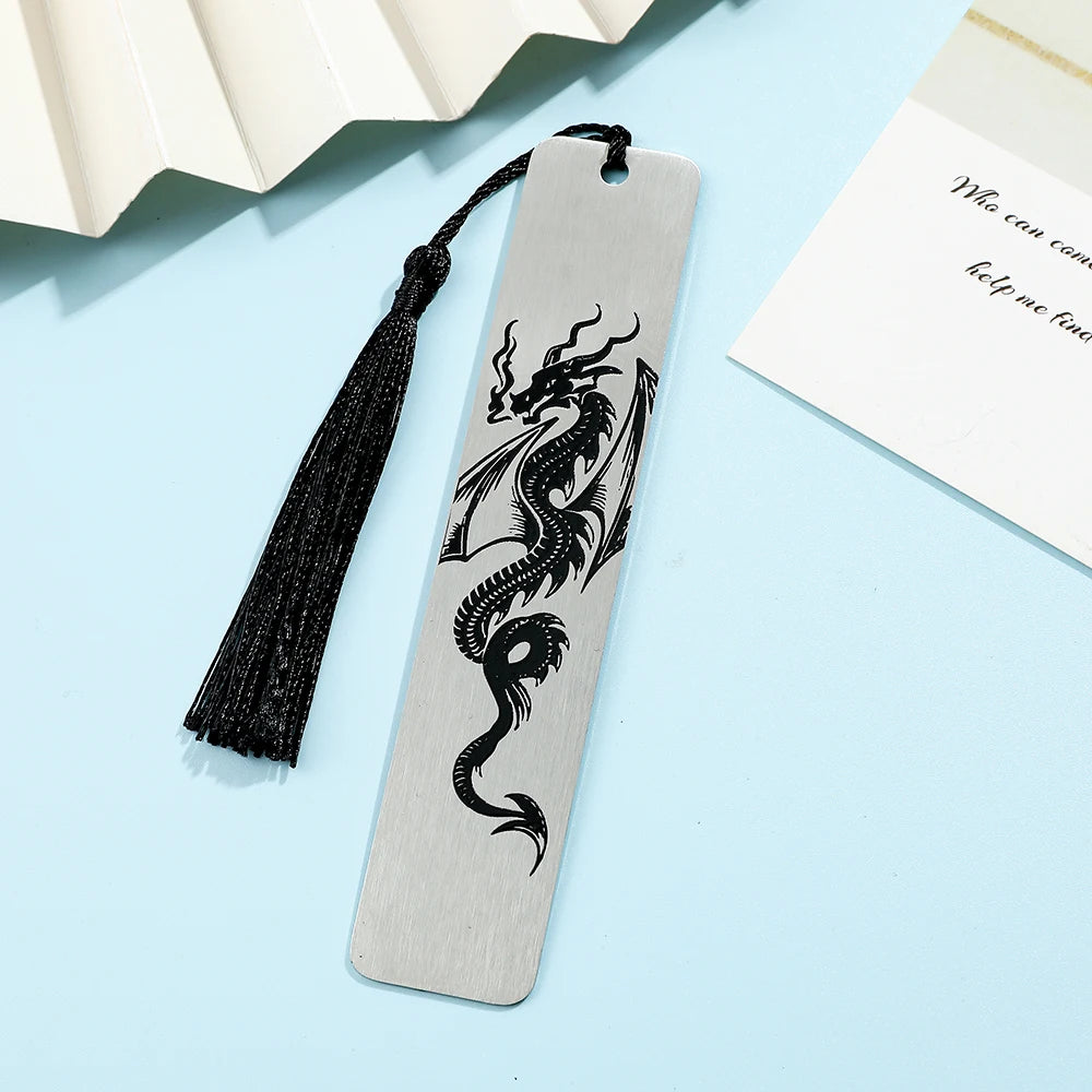 A silver metal bookmark featuring a black dragon design with a black tassel on a light blue background.