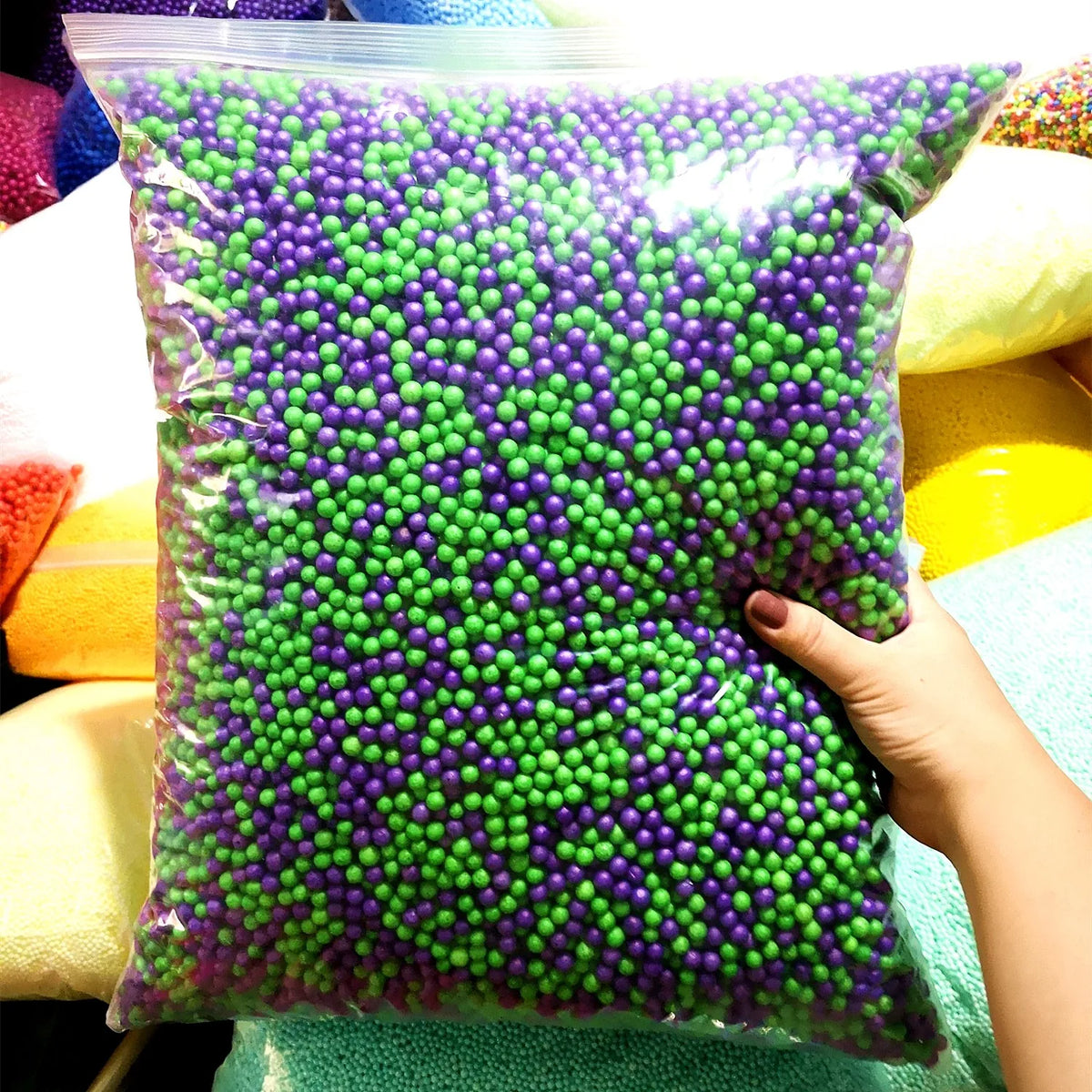 A bag filled with purple foam beads for crafting and decoration, held by a hand.