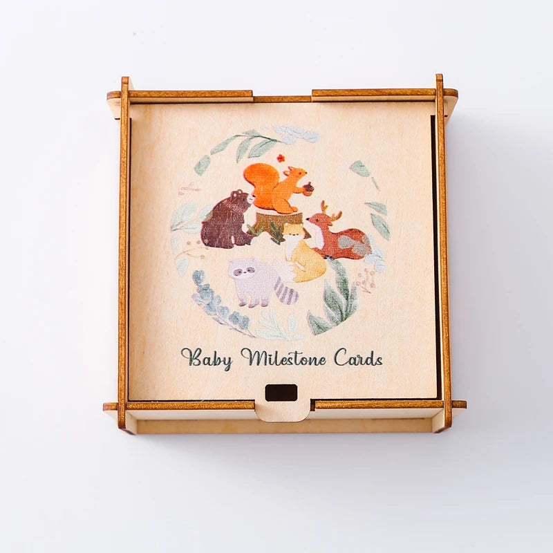 A wooden keepsake box for baby milestone cards featuring painted animals and greenery.