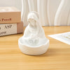 A white resin statue of the Virgin Mary with a veil and halo, displayed on a wooden table next to some books.