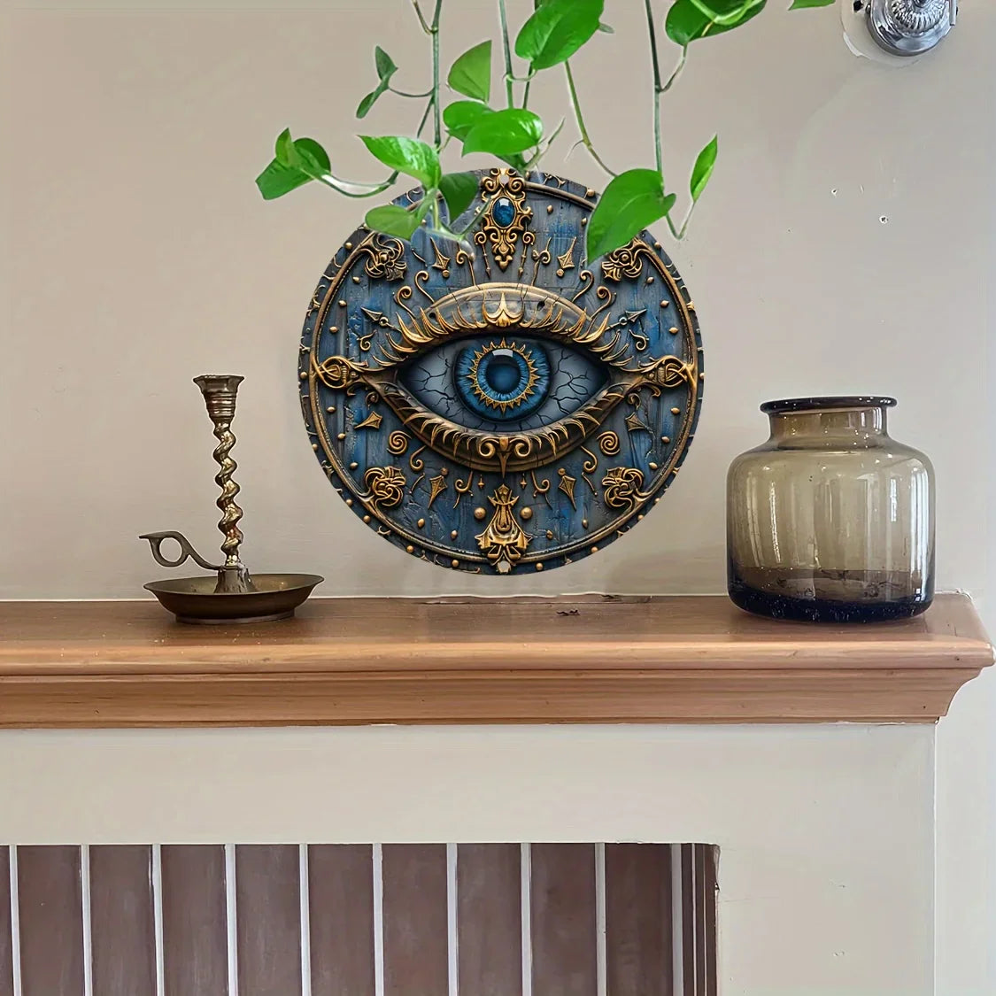 A decorative metal wall art piece featuring a blue and gold ancient Egyptian all-seeing eye surrounded by foliage.