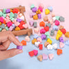 A hand is dropping various colored silicone heart beads onto a light blue surface.