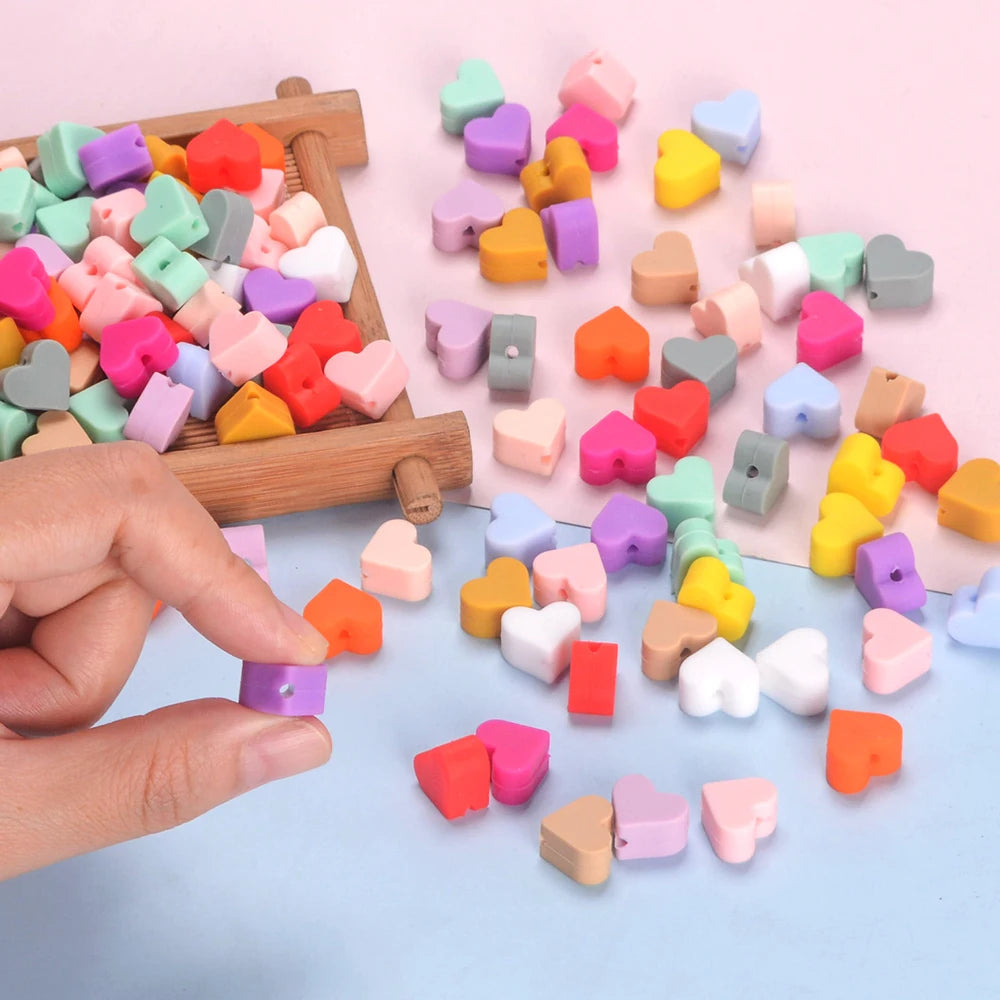 A hand is dropping various colored silicone heart beads onto a light blue surface.