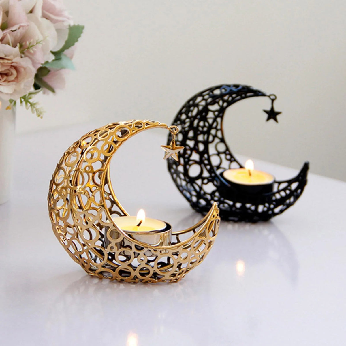 A gold crescent moon candle holder and a black crescent moon candle holder are displayed on a white surface.