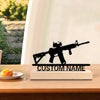 A black metal rifle statue with a wooden base is displayed on a wooden desk.