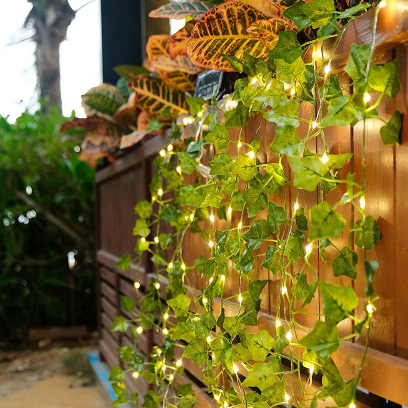 Green artificial leaves draped with warm string lights on a wooden panel for home decor