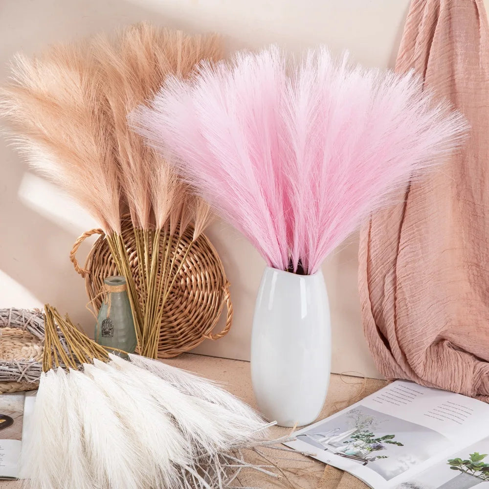 A collection of artificial pampas grass stems in various shades of pink and beige displayed on a wooden surface.