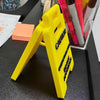 A bright yellow plastic desk sign with black lettering is shown on a dark surface.
